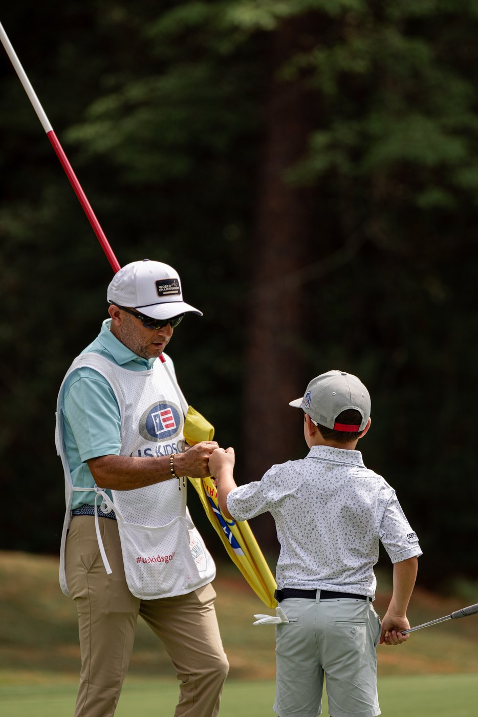 Caddie holding the flagstick while a junior golfer hands over the putter