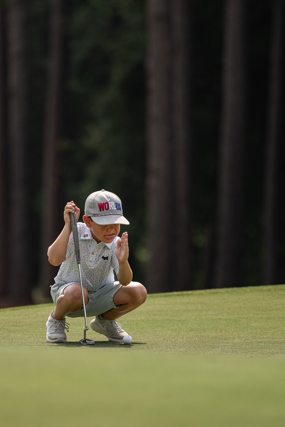 Junior golfer crouched low behind the ball, leaning on the putter to read the line