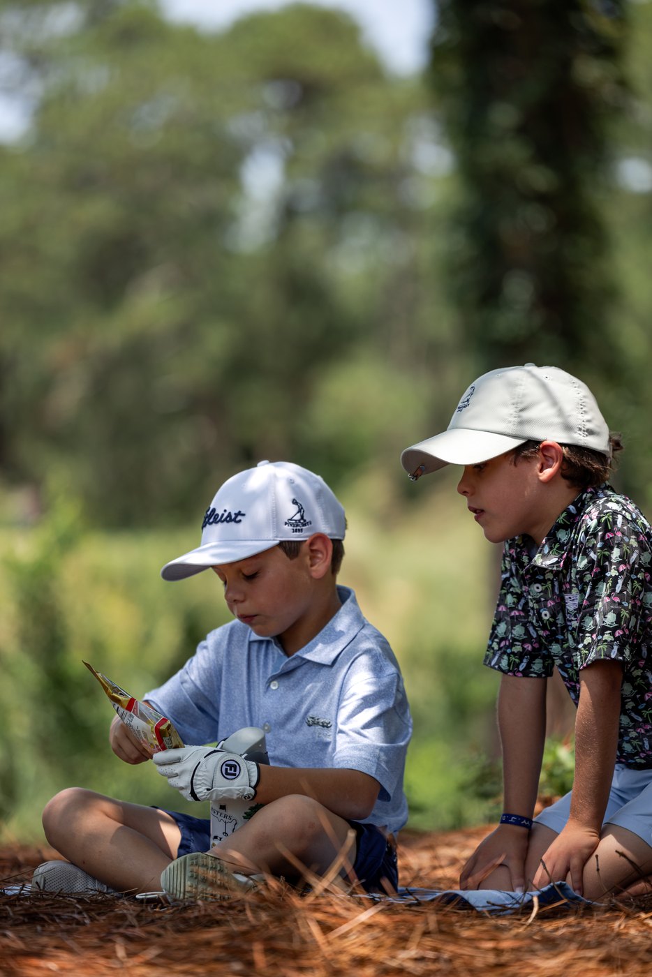 Two juniors kneeling in the pine straw looking for a ball