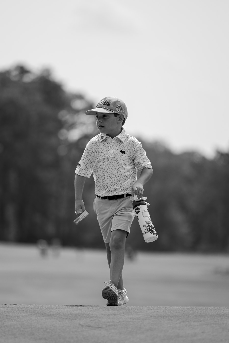 Junior golfer walking up the hole carrying a water bottle, black and white