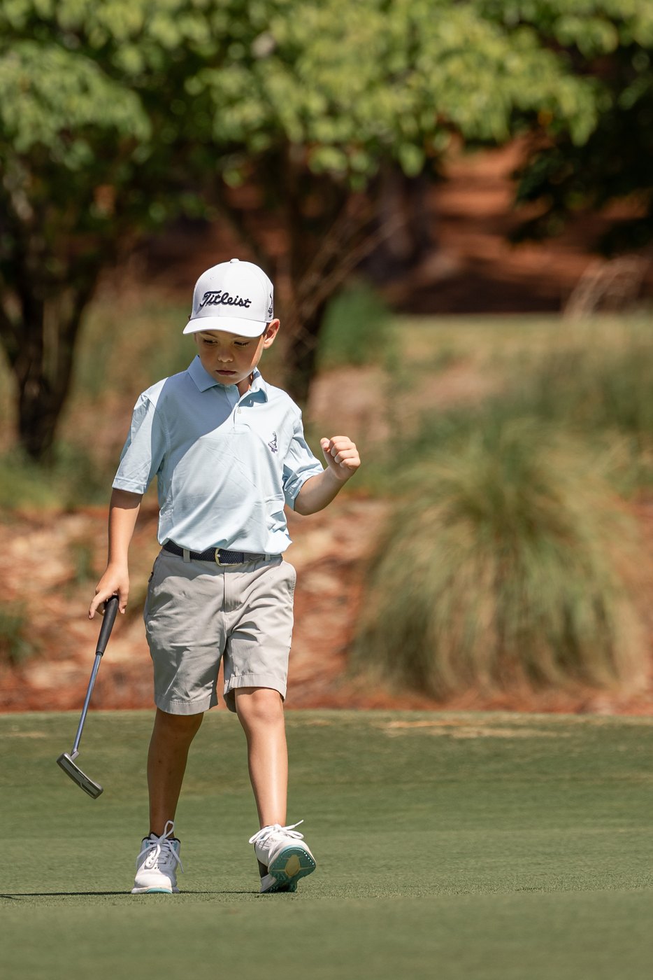 Junior golfer punching the air as he walks off the green, putter in hand