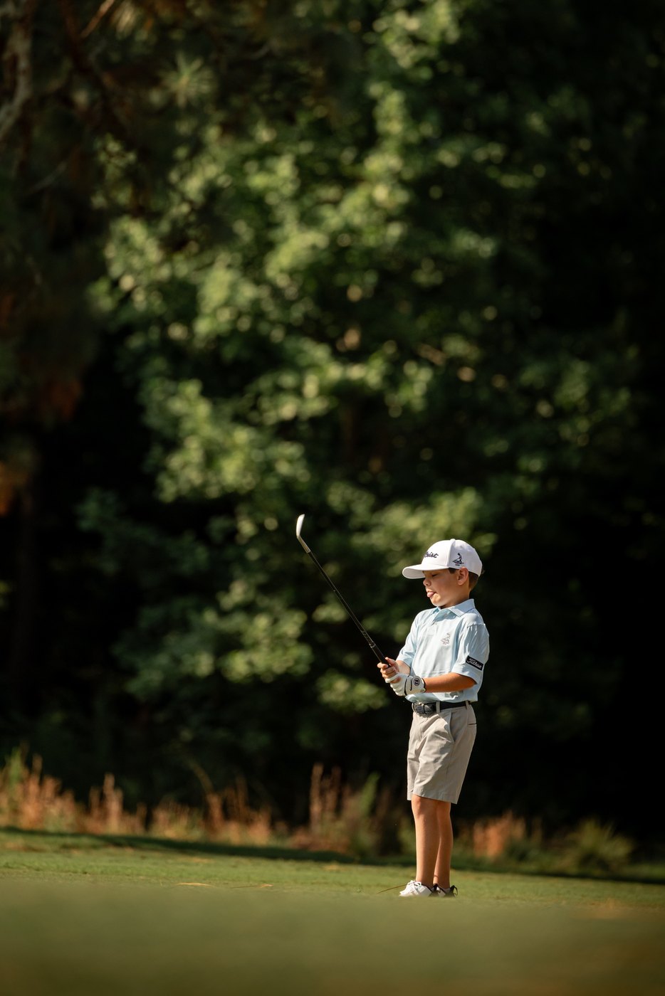 Junior golfer tossing grass to read the wind against a dark treeline