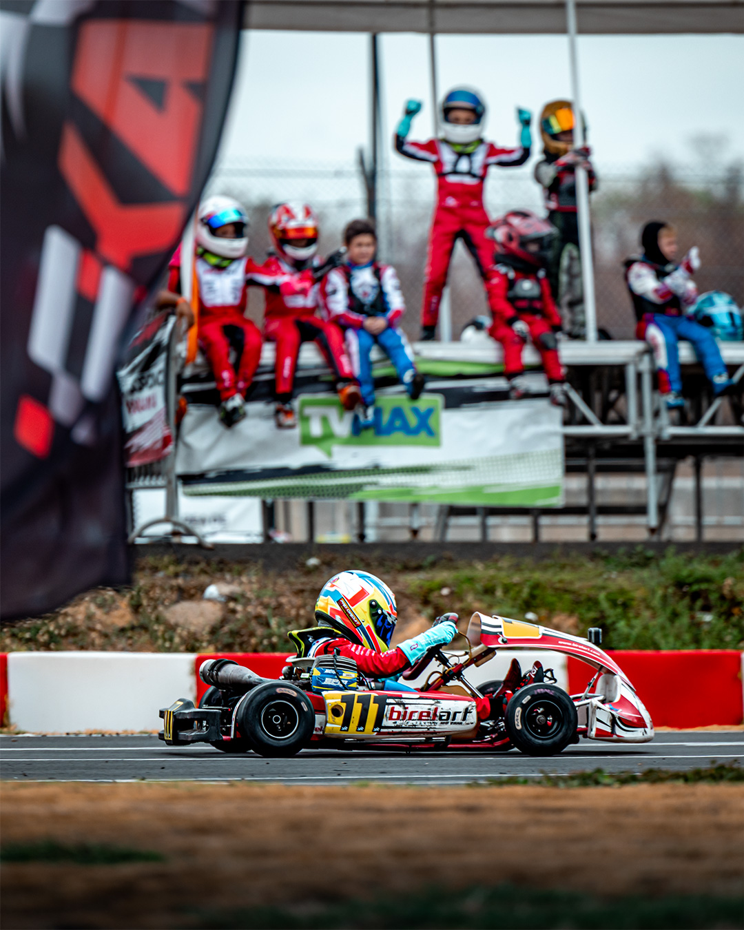 Kart crossing the line while teammates celebrate from the fence